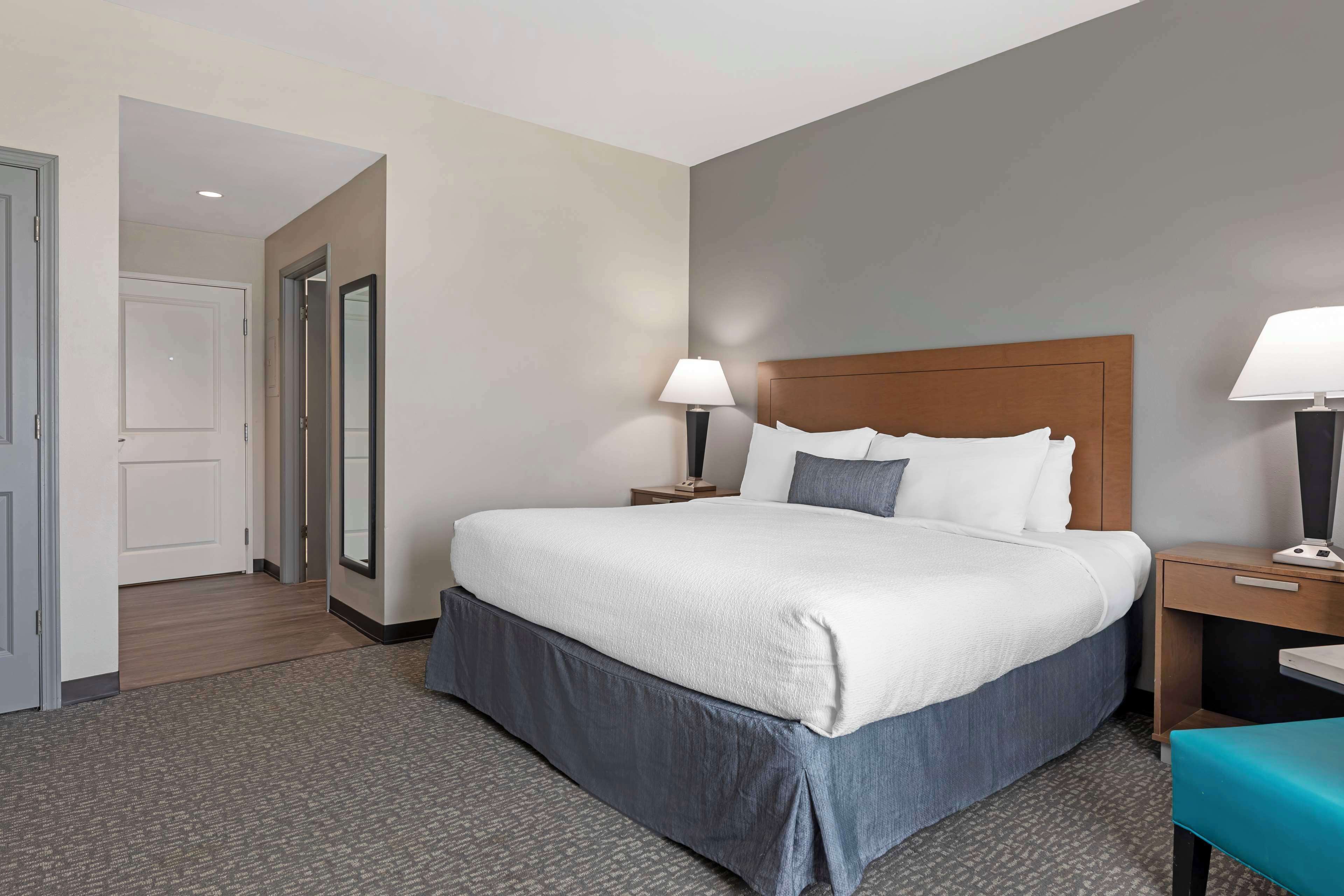 Une chambre d’hôtel avec un grand lit, deux tables de chevet avec des lampes, une tête de lit en bois et un sol recouvert de moquette.