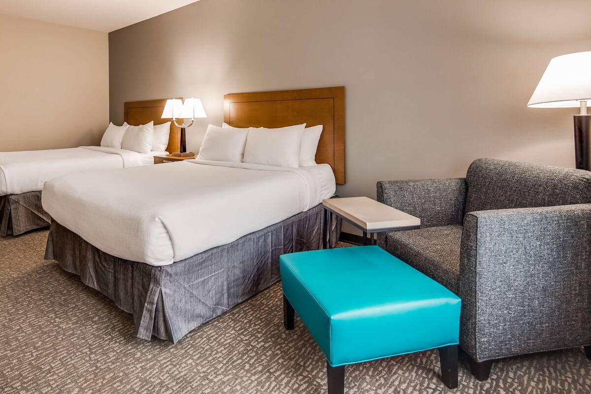 Een hotelkamer met twee bedden, een kleine tafel, een blauwgroene bank en een grijze fauteuil.