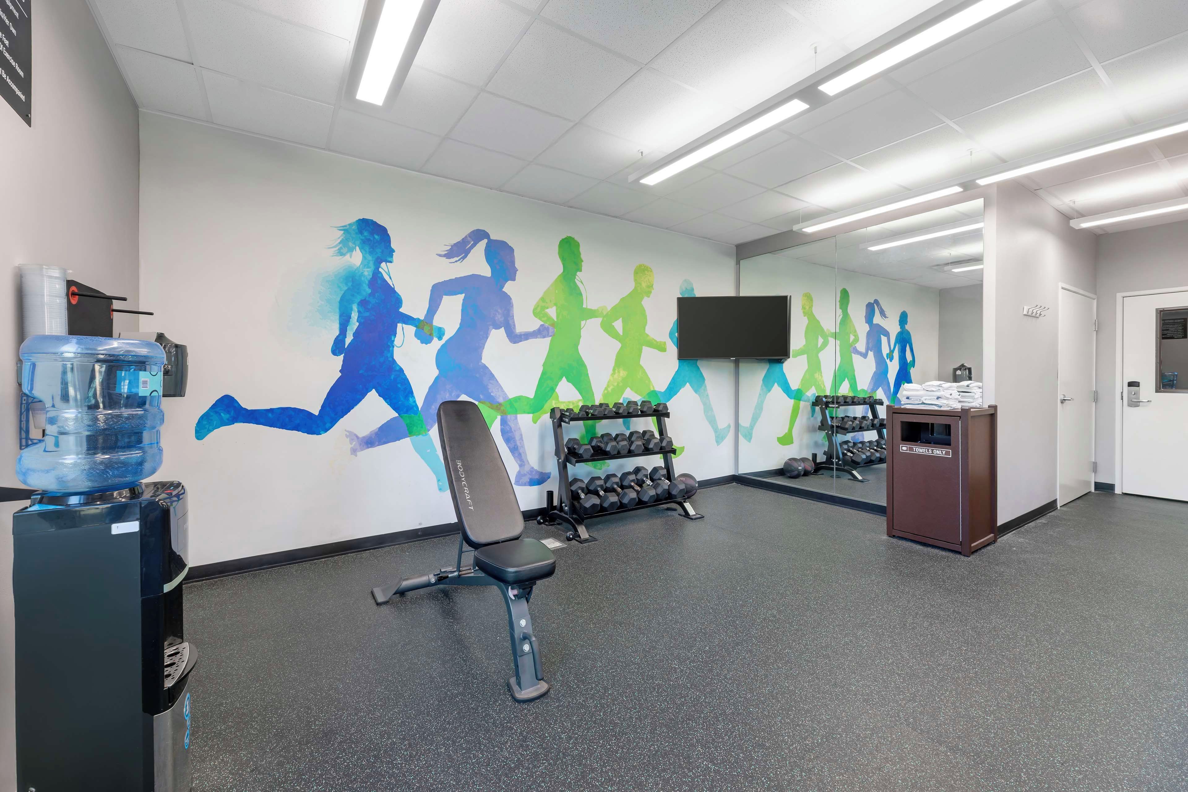 A gym with exercise equipment, a water dispenser, and a wall with silhouettes of runners.