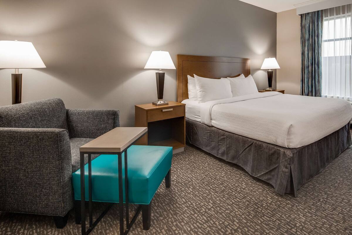 Een hotelkamer met een bed, twee nachtkastjes met lampen, een bank, een klein tafeltje en een raam met gordijnen.