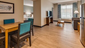 Een hotelkamer met een eethoek, televisie, bank en raam met gordijnen.