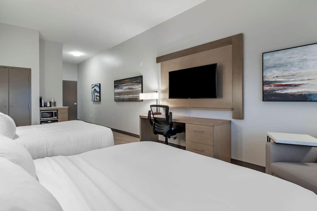 Ein Hotelzimmer mit zwei Betten, einem Schreibtisch, einem Sessel, einem Fernseher und Bildern an den Wänden.