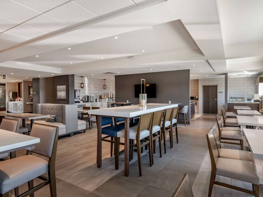 A modern hotel lobby with a long reception desk, seating areas, and a large flat-screen TV mounted on the wall.