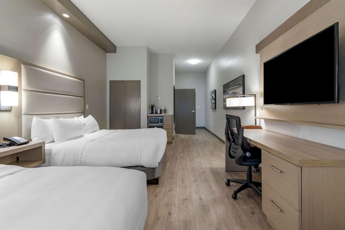 Ein Hotelzimmer mit zwei Betten, einem Schreibtisch, einem Flachbildfernseher und einer Schreibtischlampe.
