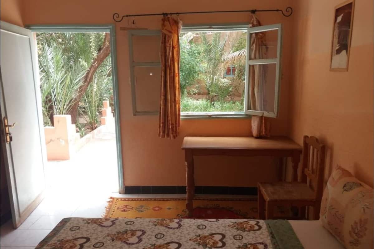 A bedroom with a bed, a wooden desk, a chair, and a window with curtains.