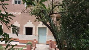 A building with a tiled facade, a blue door, and a pathway leading to it. - Maison d'Hôtes au Jardin de Tamnougalt (Mezguita)