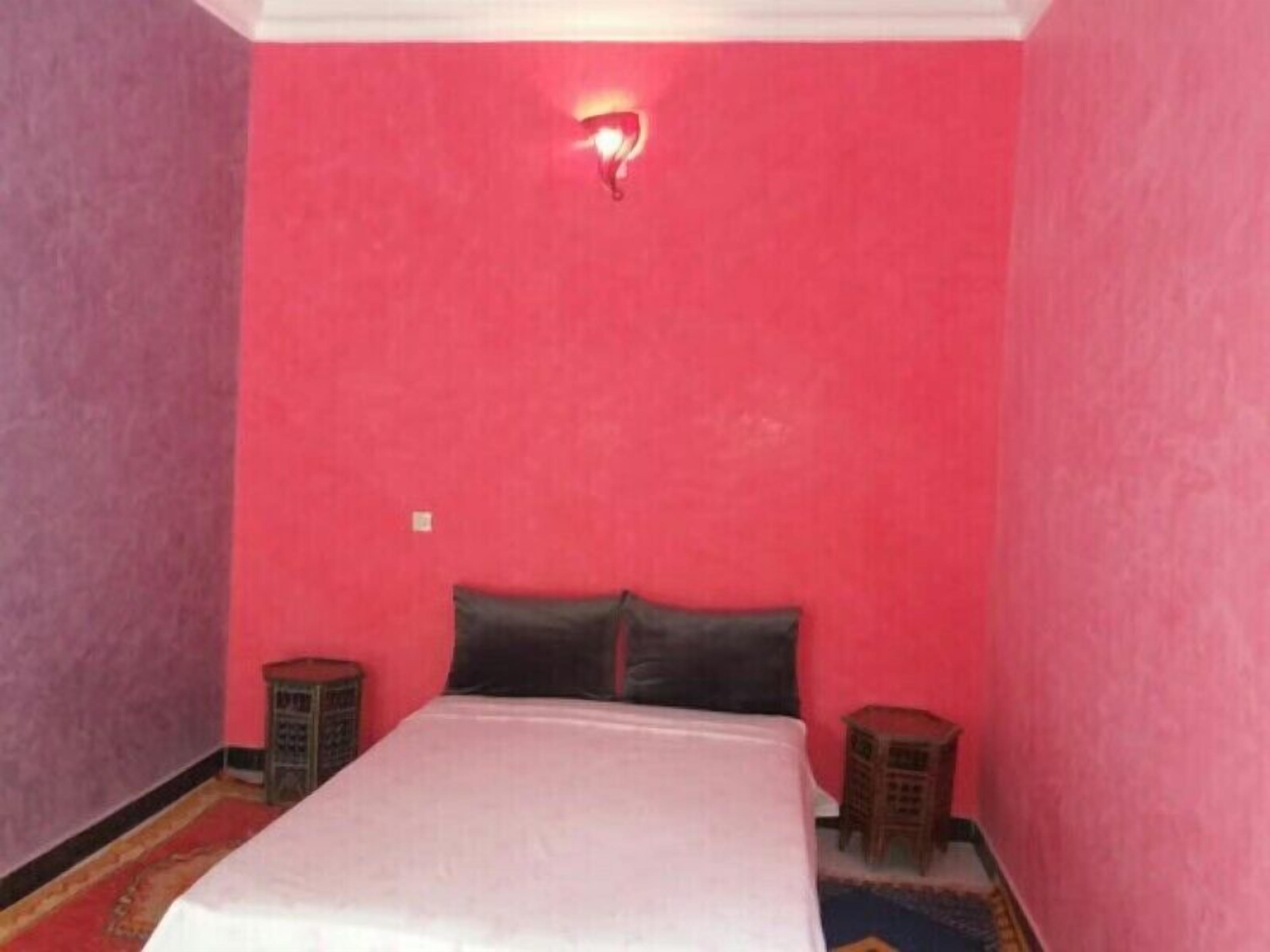 Un dormitorio con una cama individual, una pared roja y una mesita de noche pequeña.