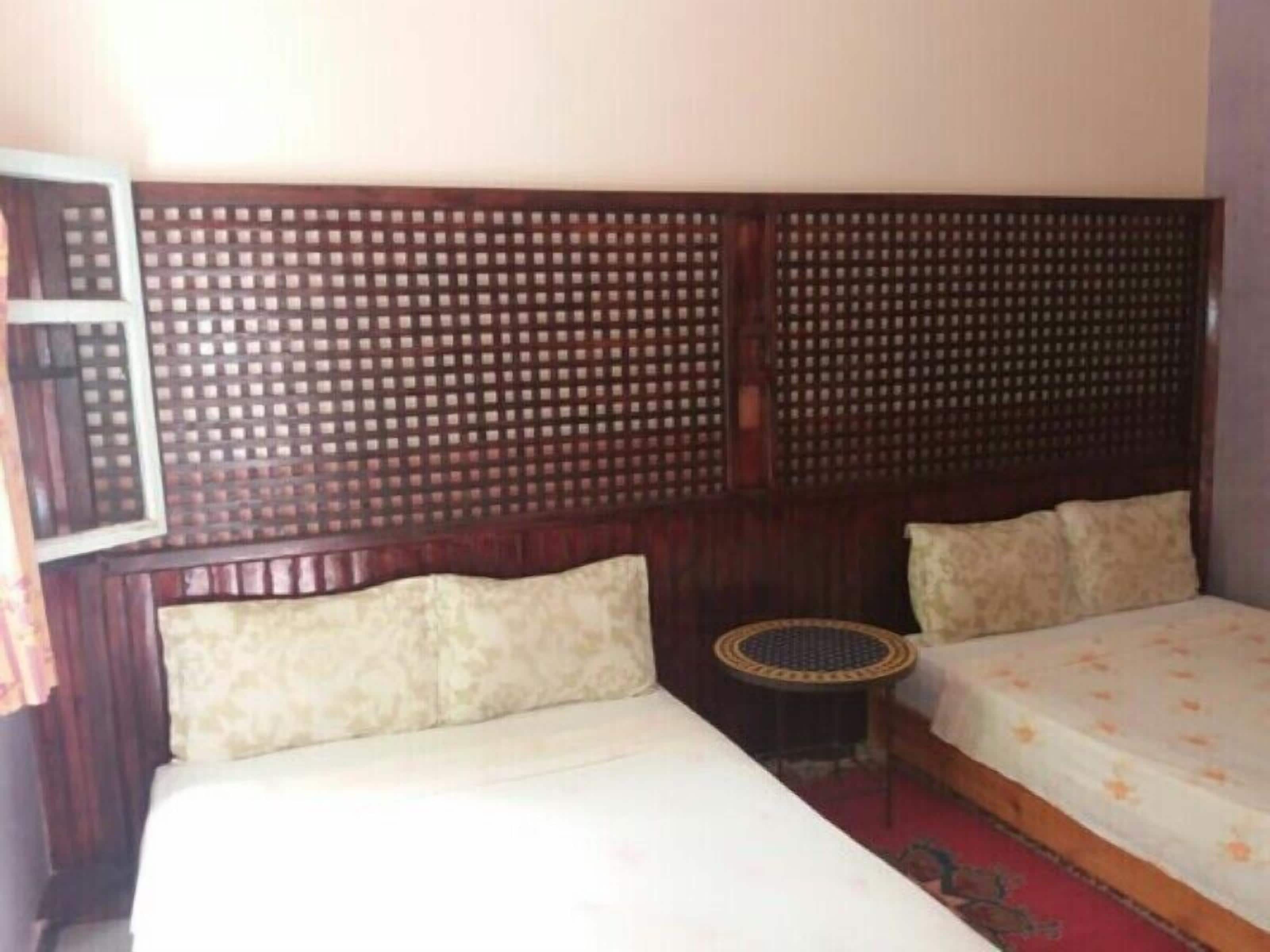 A room with two beds, a wooden headboard, a small round table, and a patterned rug.