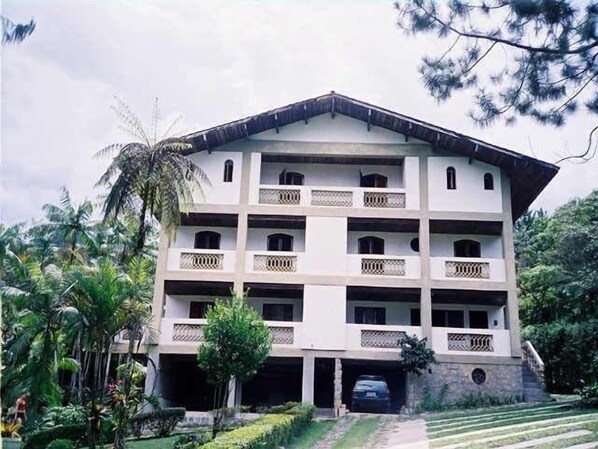 A multi-story building with balconies, a covered parking area, and lush greenery around. - House in Serrinha, near Penedo and very close to Camping Club do Brasil (Resende)