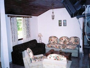 Relax in this inviting living room with a sofa, armchair, and table, surrounded by framed artwork and natural light.