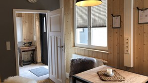 Una habitación acogedora con detalles de madera, una mesa con una taza, un sillón mullido, una máquina de coser y una ventana con persianas.