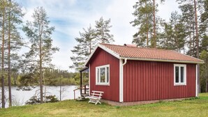 A small red cabin with a porch and a bench, surrounded by trees and a lake. - Cozy home in Bodafors with kitchen (Bodafors)
