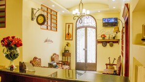 Habitación bien iluminada con un espejo grande, un reloj y un televisor en la pared. Hay sillas y una mesa con un jarrón de flores.