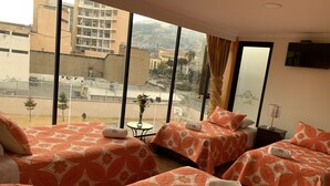Una habitación de hotel con dos camas, una mesita con un florero y un televisor en la pared.