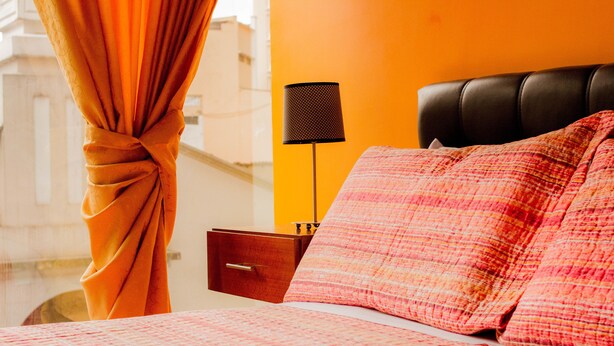 Quarto de hotel com cama, mesa de cabeceira, luminária e vista para a cidade.