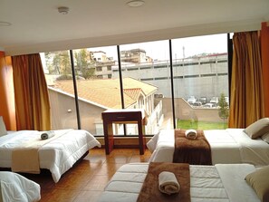Habitación de hotel con dos camas, una mesita y un ventanal grande con vistas a edificios y un puente.