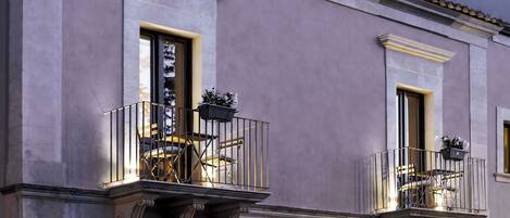 A building with two balconies, each with a chair and a potted plant.