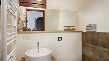 A bathroom with a white sink, wooden countertop, and a mirror above it. There is a window with a wooden frame and a towel rack with towels.