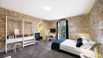 A bedroom with a stone wall, a bed, a desk, a chair, and a small table.