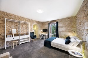 A bedroom with a stone wall, a bed, a desk, a chair, and a small table. - Centosedici Rooms (Ragusa)