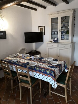 A dining area with a table set for four, a cabinet with dishes, and a television mounted on the wall.