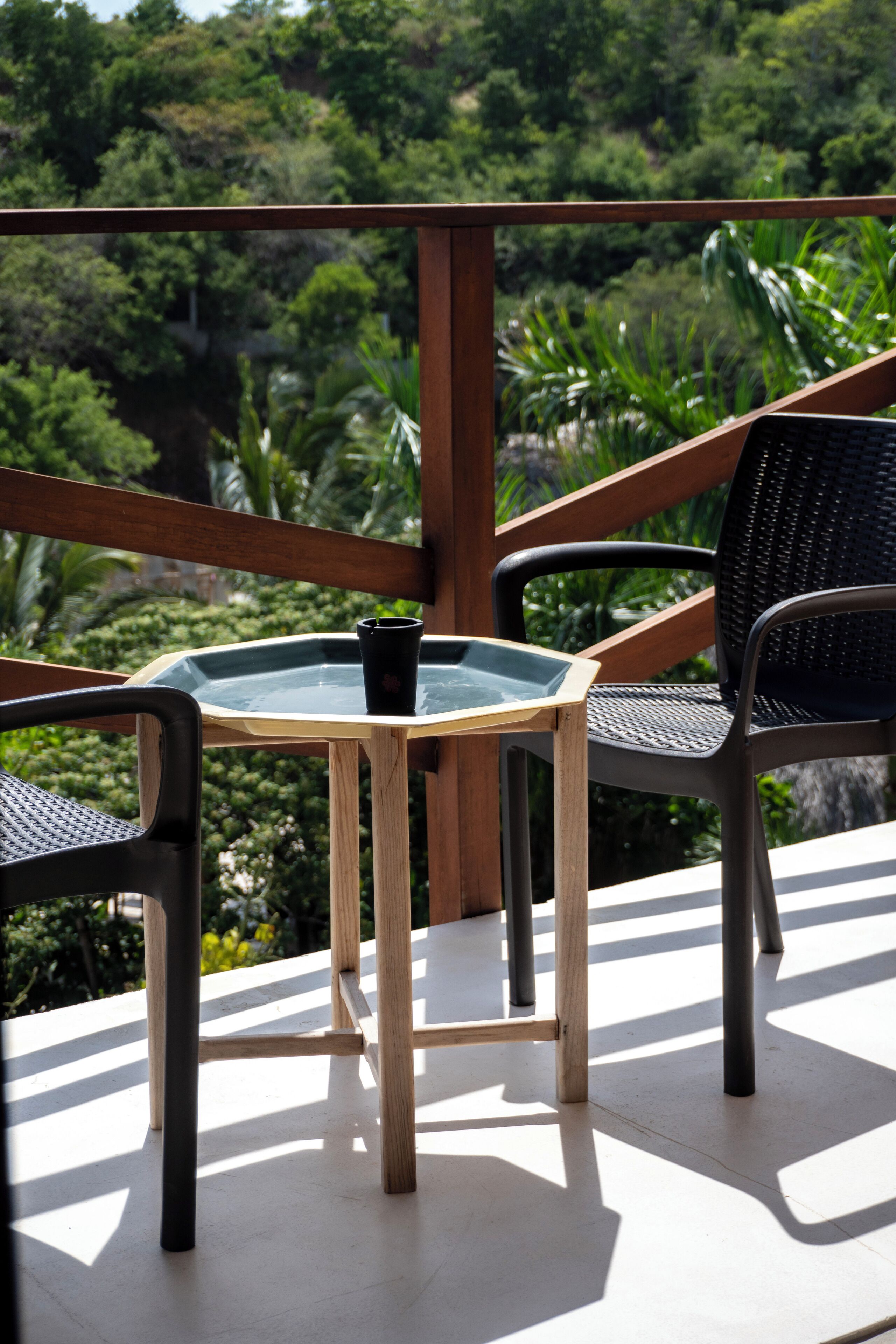 A balcony with a glass table, two chairs, and a potted plant.
