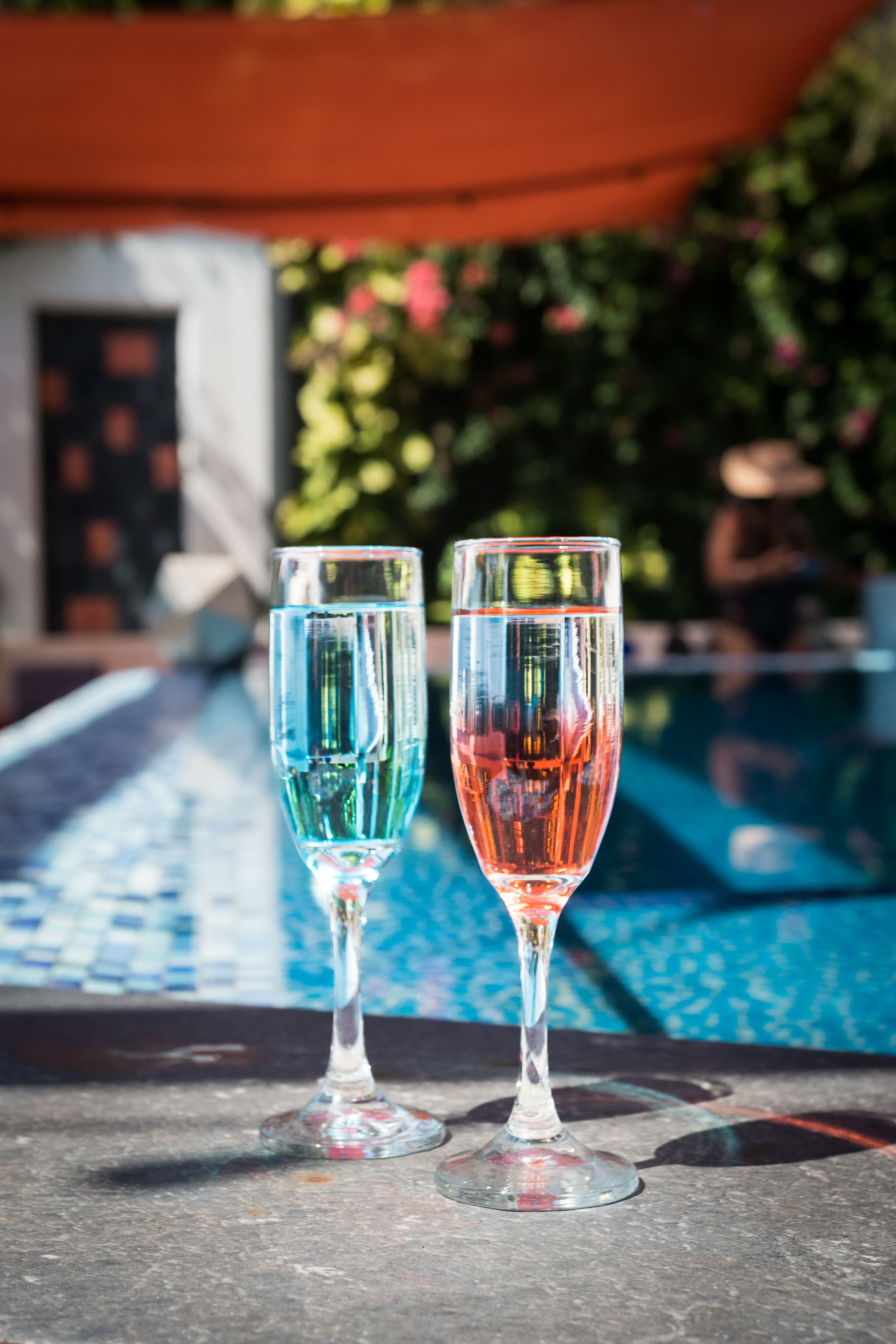 Deux coupes à champagne remplies d’eau sont posées sur une table près d’une piscine.