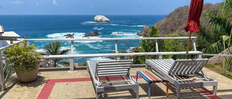 A balcony with a view of the ocean, featuring a wooden bench and a red umbrella.