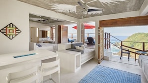 A modern bedroom with a bed, a desk, and a chair. There is a balcony with a view of the ocean.