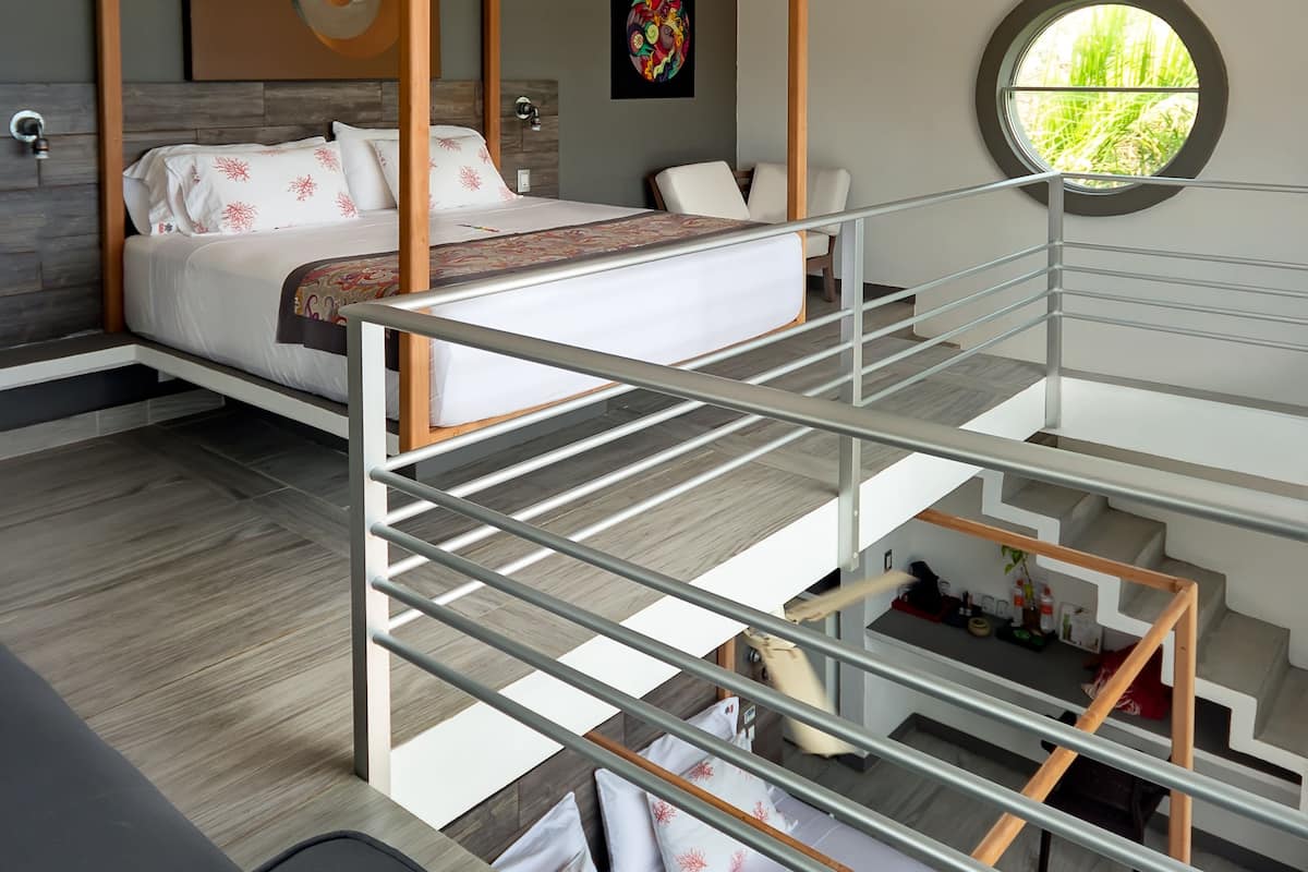 A bedroom with a four-poster bed, a staircase, and a view of greenery through a window.