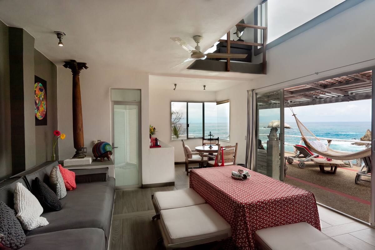 A modern interior with a dining area, a sofa, and a balcony with a view of the sea.