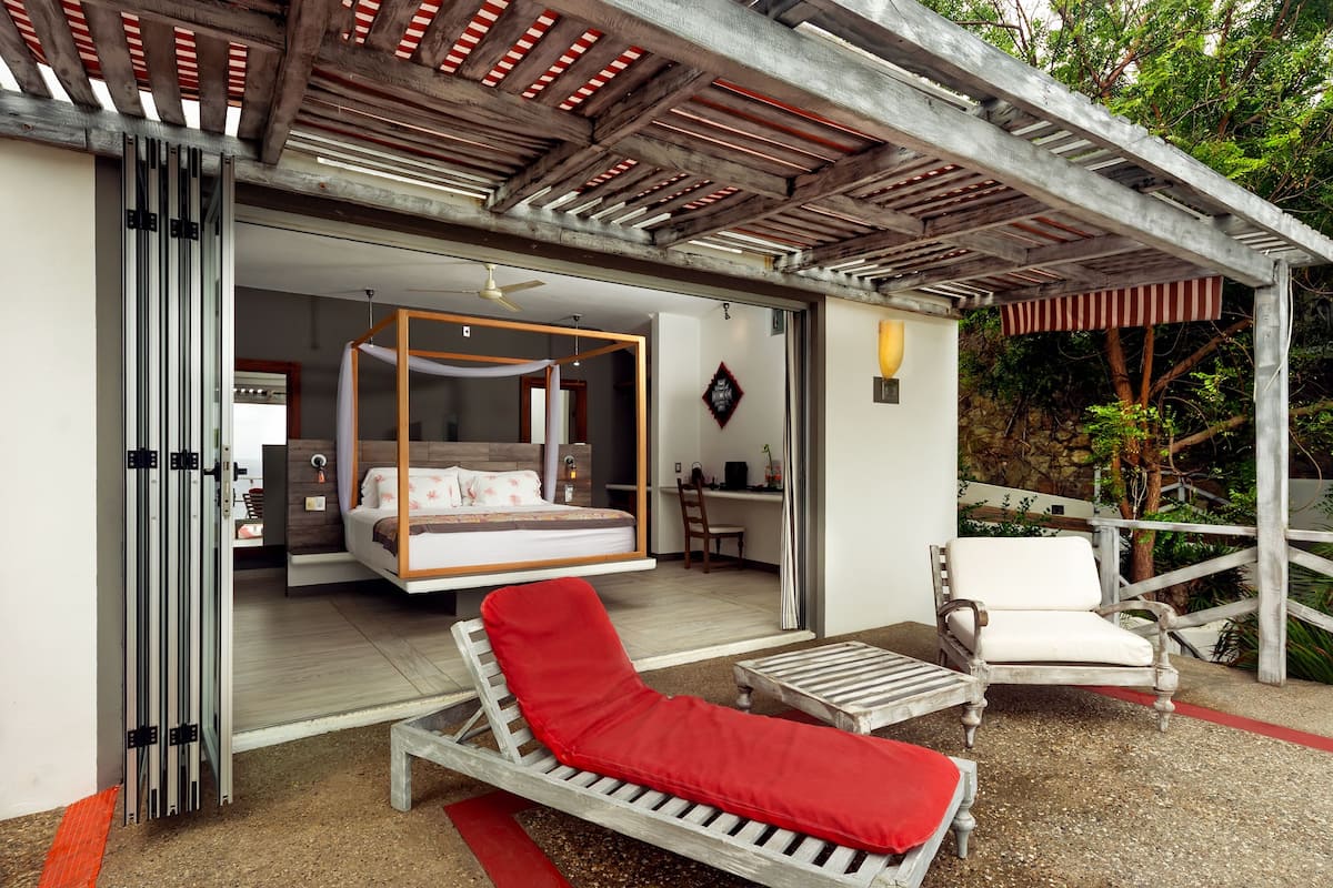 A bedroom with a canopy bed, a sitting area with a red cushion, and a wooden chair.