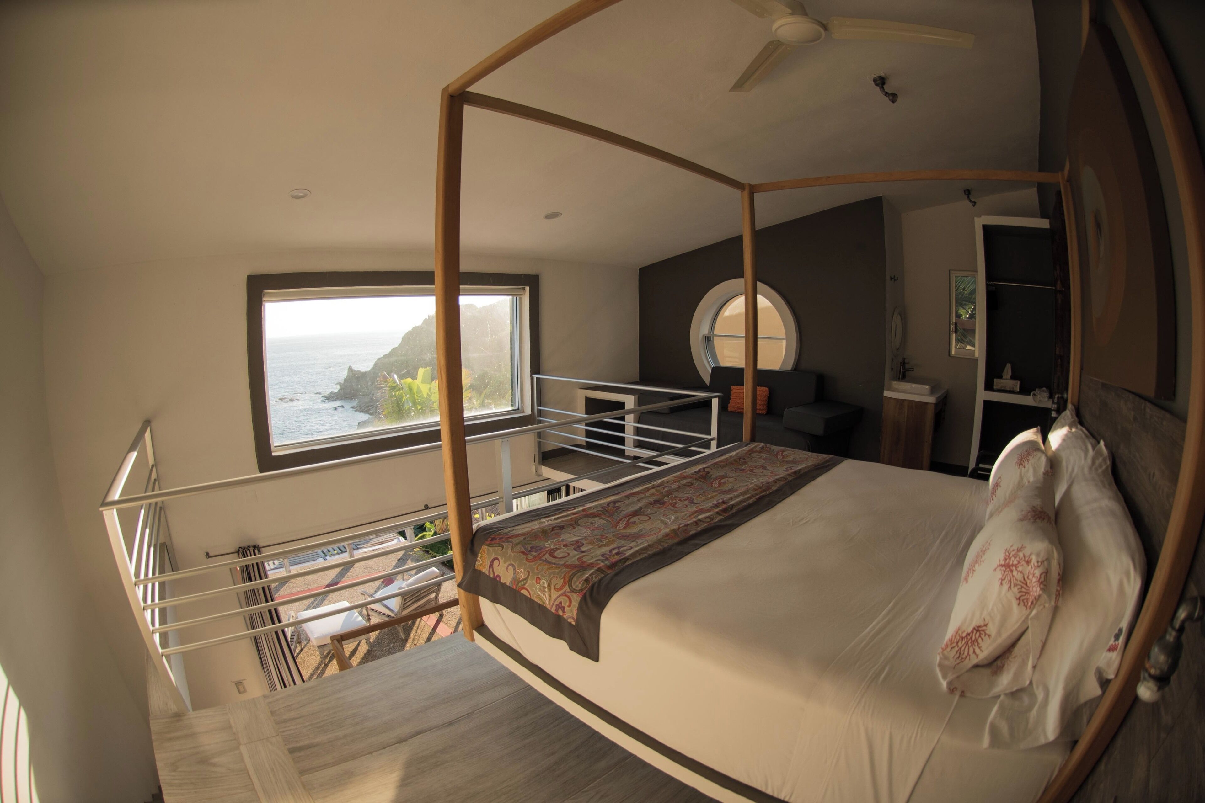 Un dormitorio con cama con dosel, vistas al océano, un balcón y un ventanal redondo.