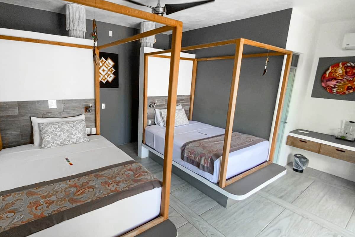 A modern bedroom with two beds, each with a wooden frame and white bedding. There is a small bedside table with a lamp and a decorative wall hanging.
