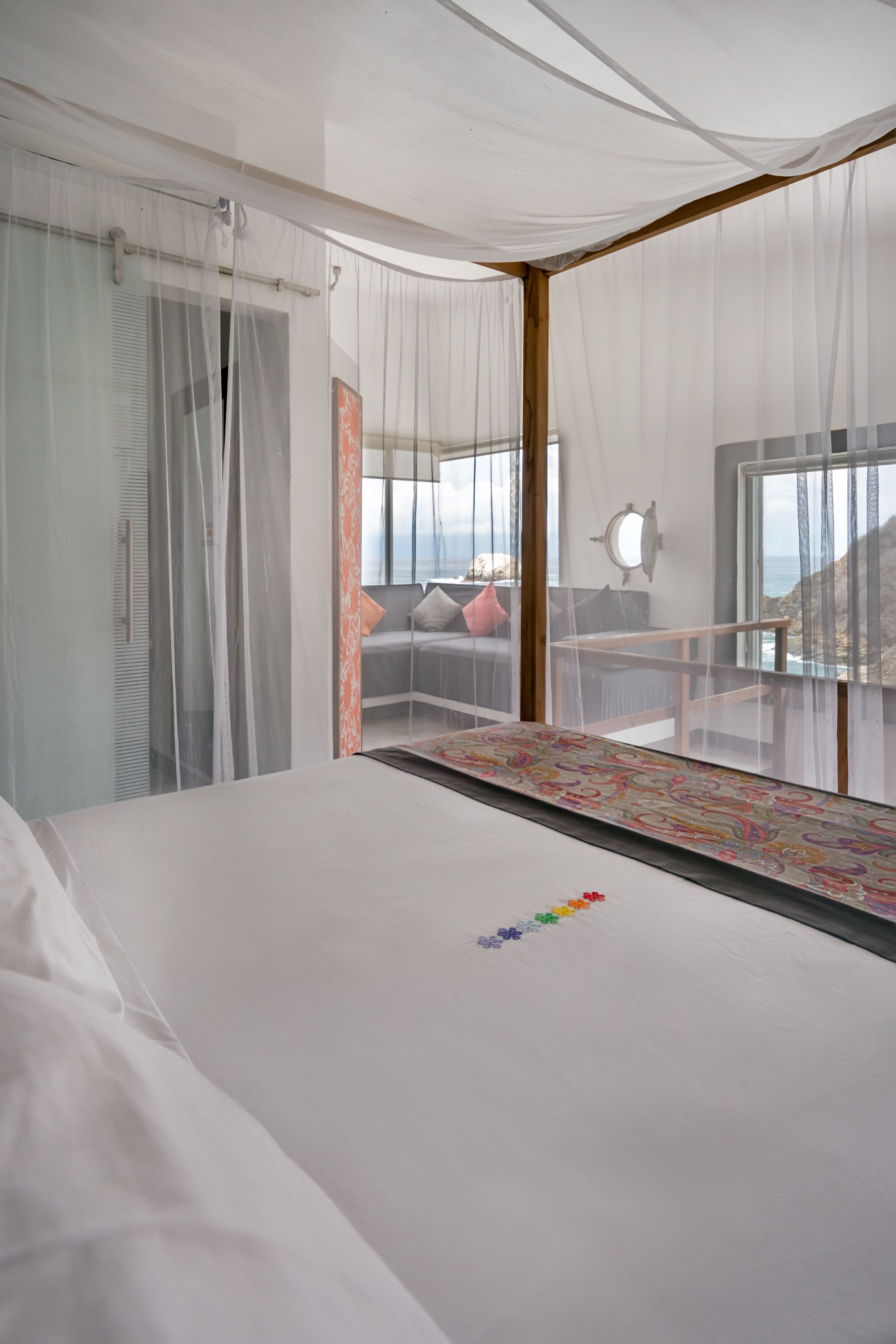 A bedroom with a large bed, a view of the sea, and sheer curtains.