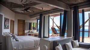A modern hotel room with a bed, a sofa, a desk, and a view of the sea.
