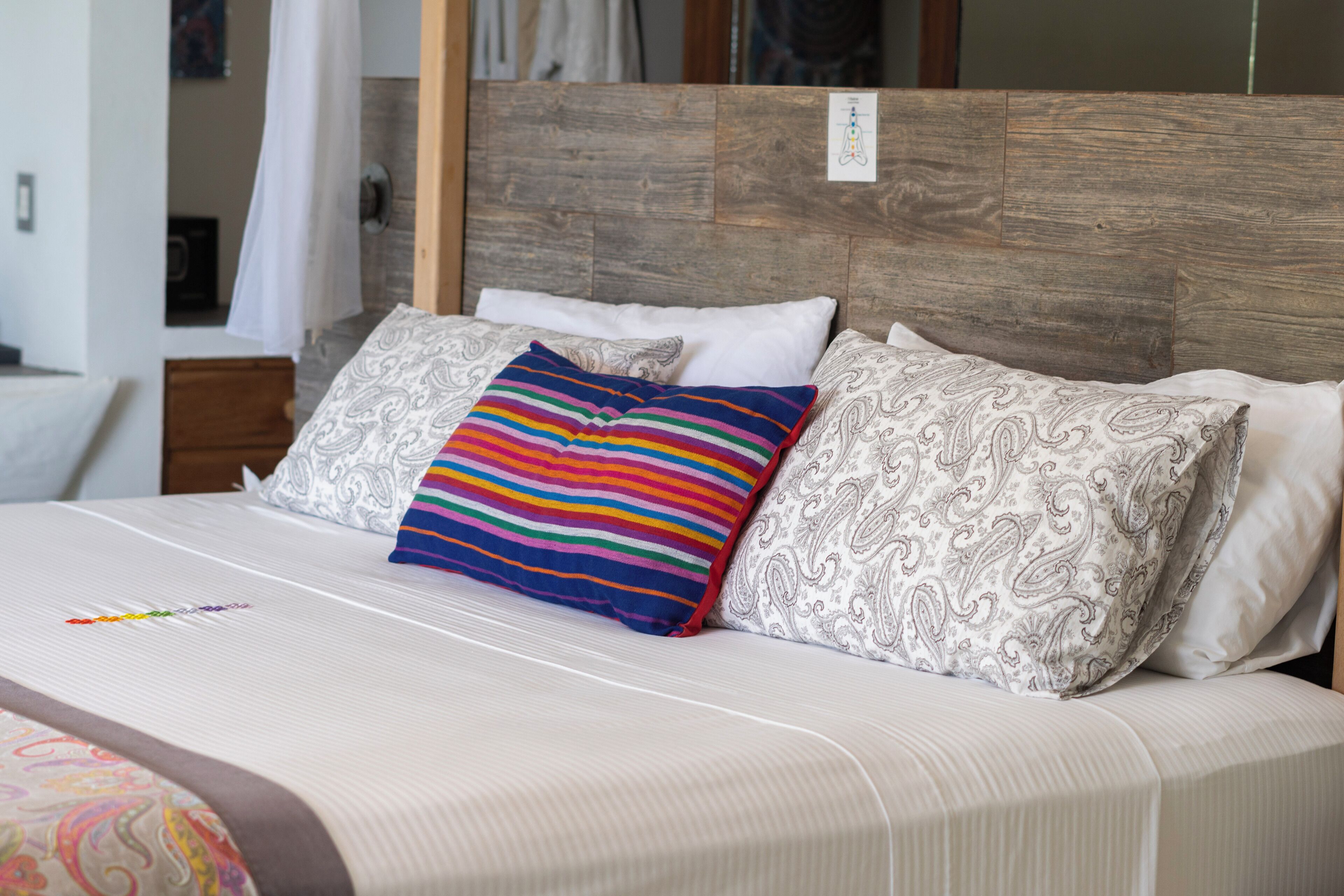 A neatly made bed with a striped pillow, a paisley pillow, and a white pillow.