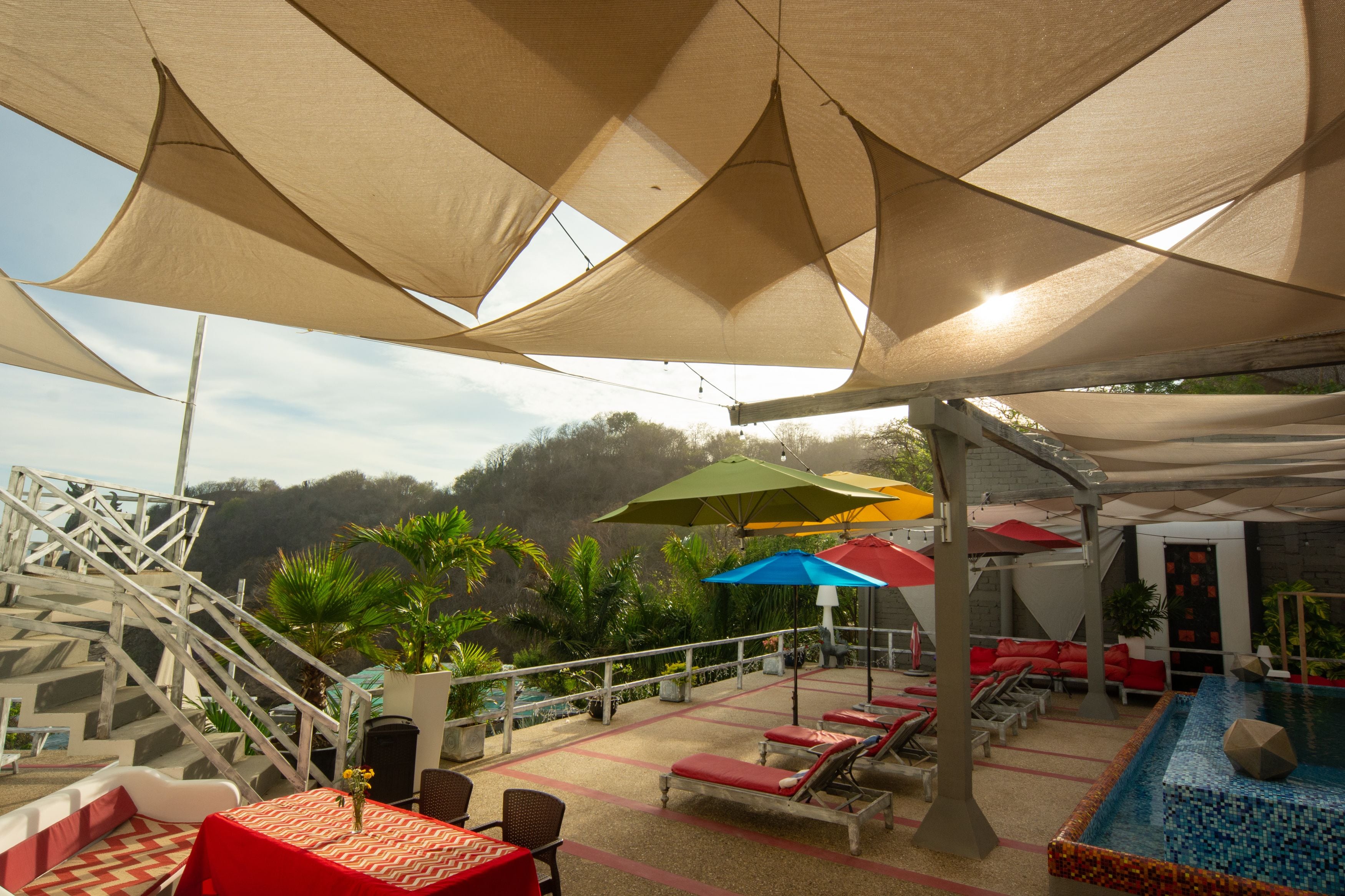 A rooftop pool area with lounge chairs, umbrellas, and a staircase leading to a higher level.