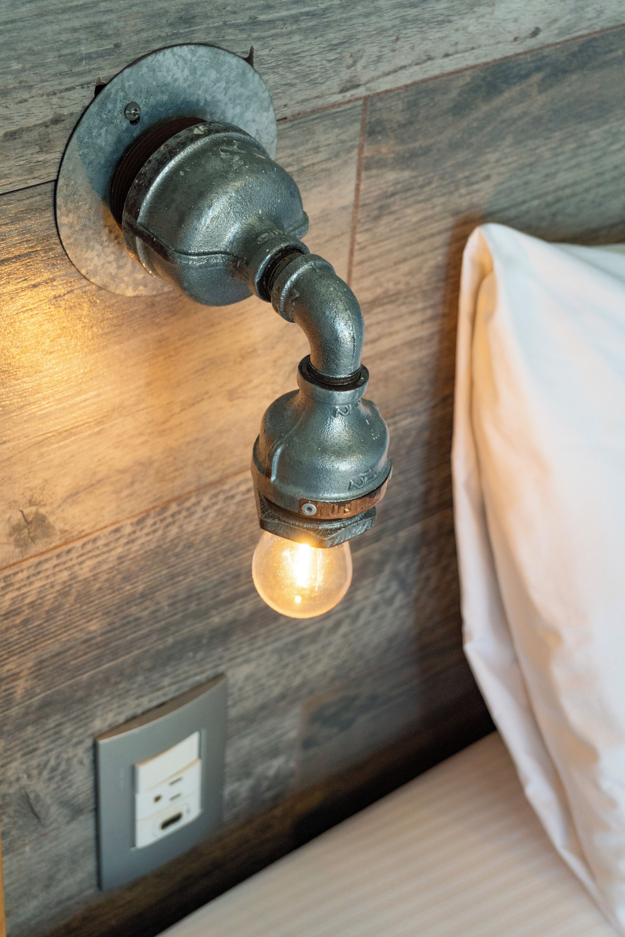 A wall-mounted light fixture with a single bulb, a power outlet, and a switch plate.
