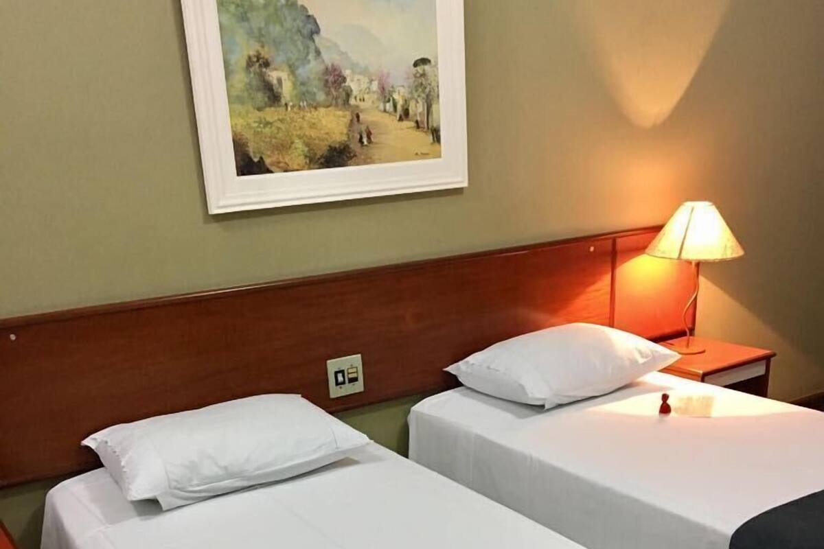 Ein Hotelzimmer mit zwei Betten, einem Nachttisch mit Lampe, einem Bild an der Wand und einem roten Teppich.
