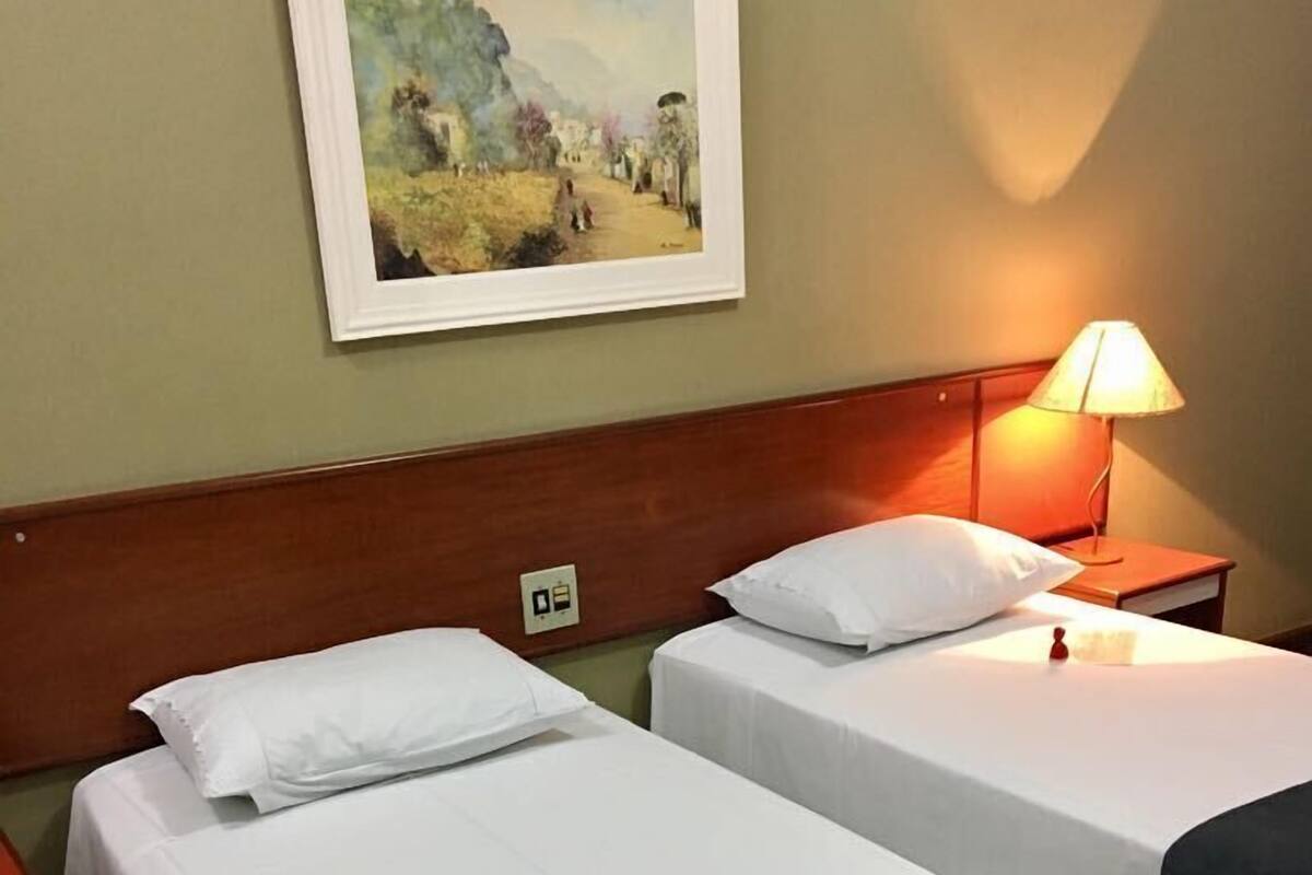 Ein Hotelzimmer mit zwei Einzelbetten, einem Holzkopfstück, einem Nachttisch mit Lampe und einem Bild an der Wand.