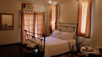 A hotel room with a bed, a chair, a table with glasses and plates, and curtains.