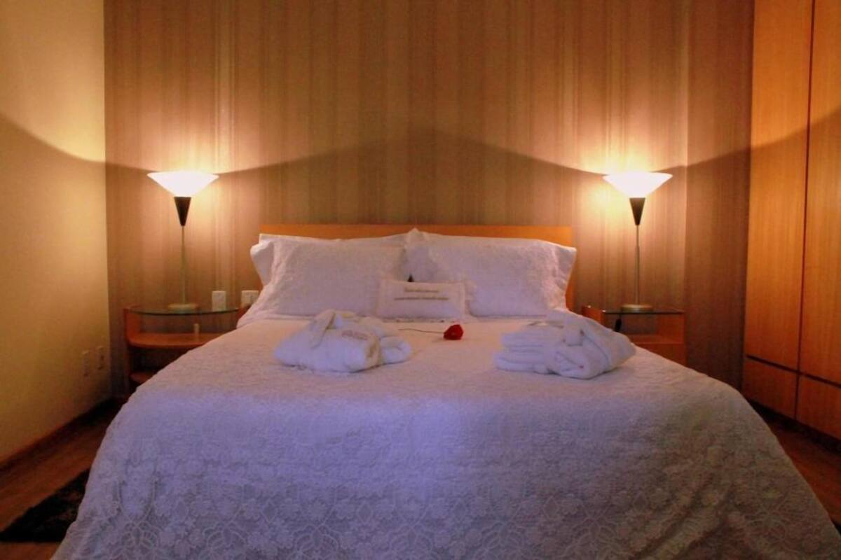 Ein ordentlich bezogenes Bett mit weißen Leinen und Handtüchern, zwei Nachttische mit Lampen und ein Holzkopfende.