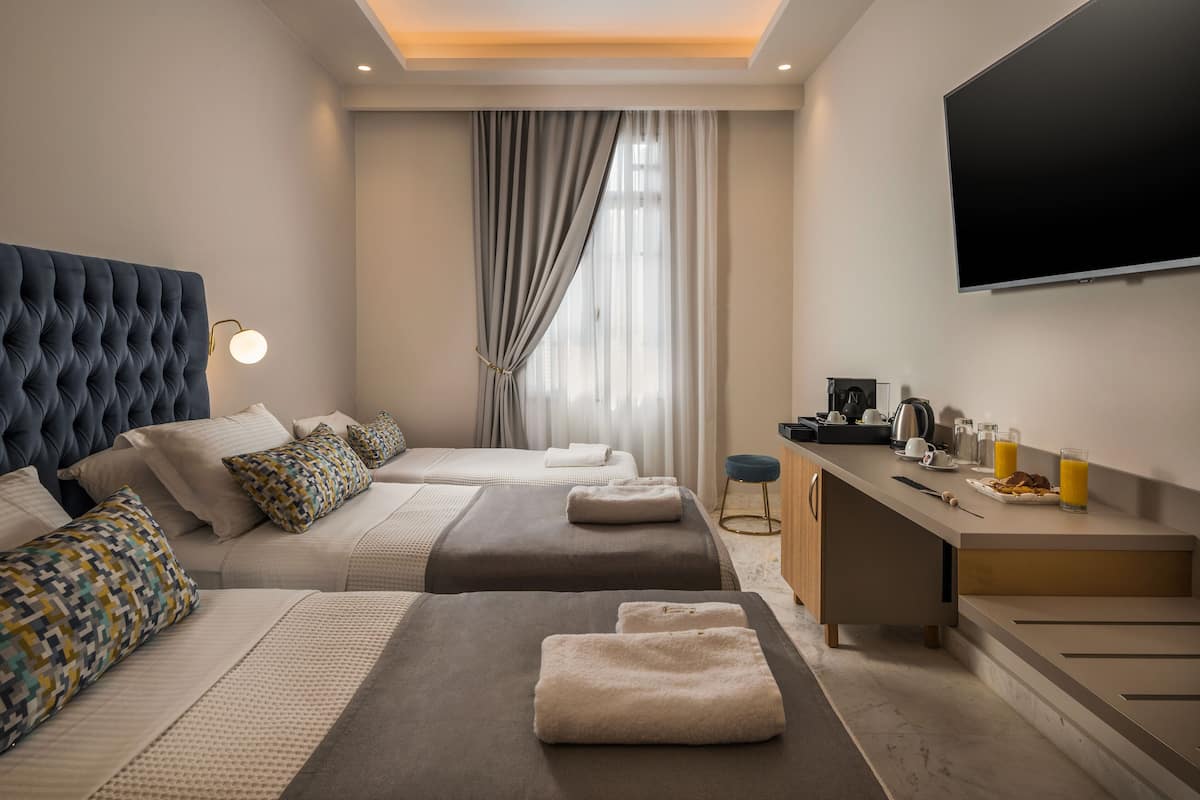 Une chambre d’hôtel avec deux lits, un bureau, un téléviseur à écran plat et une grande fenêtre avec des rideaux.
