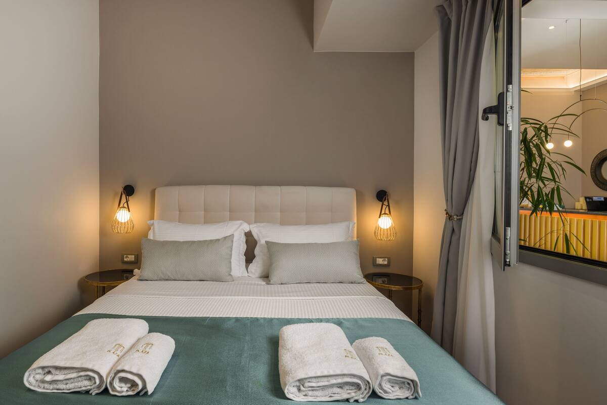 Un lit bien fait, avec deux serviettes enroulées, une couvre-lit verte et deux lampes de chevet.