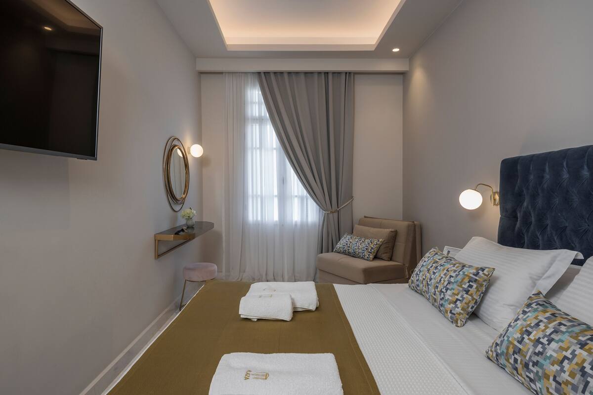 Une chambre d’hôtel avec un lit, un canapé, un téléviseur fixé au mur et une fenêtre avec des rideaux.