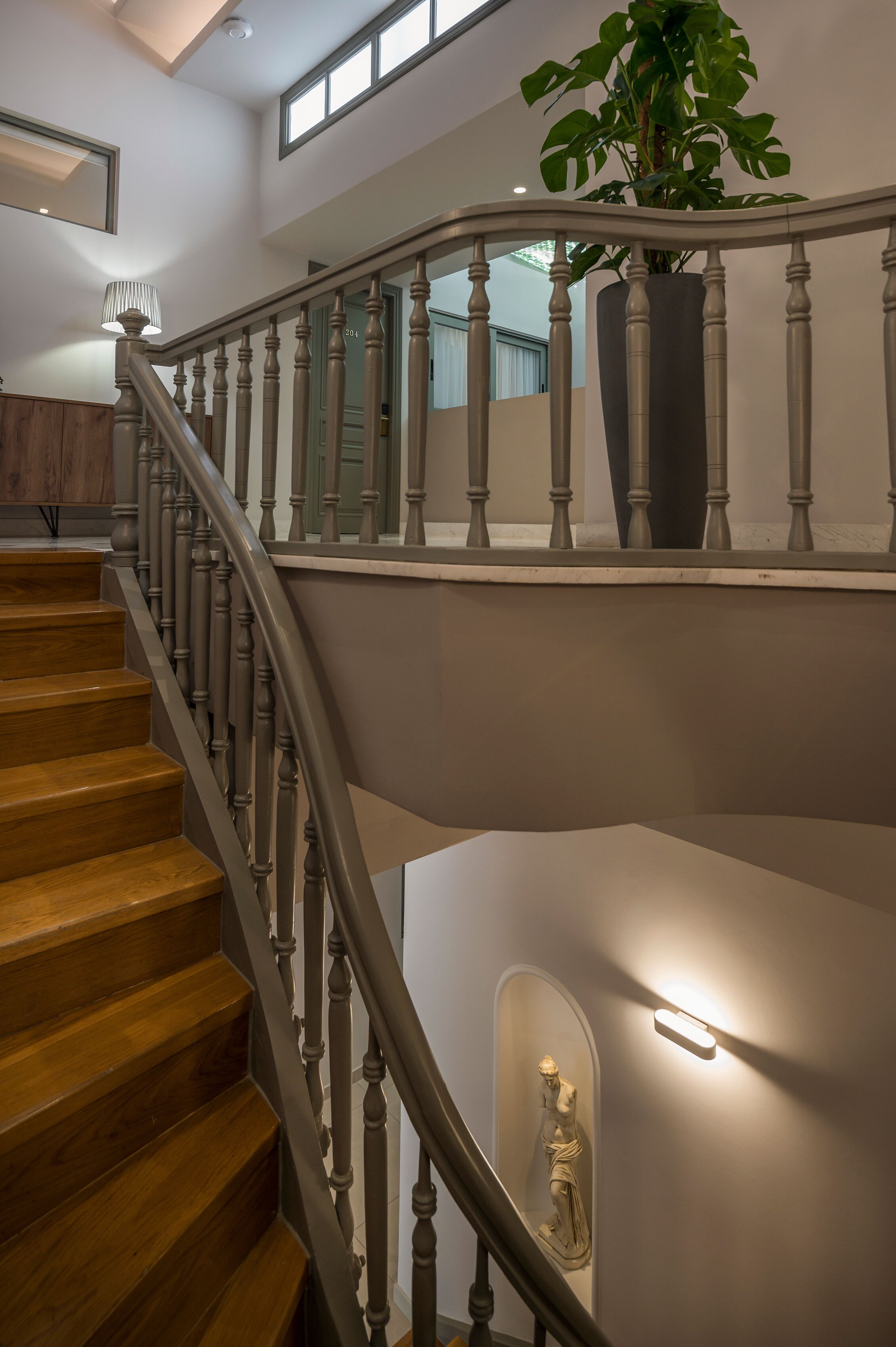 Een trap met houten treden en een balustrade, een kamerplant en een wandlamp.