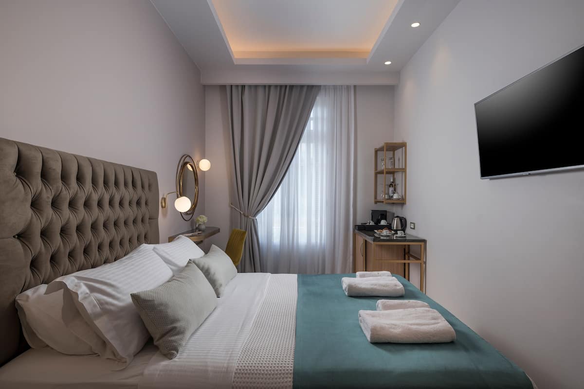 Une chambre d’hôtel moderne dotée d’une tête de lit capitonnée, d’un grand téléviseur à écran plat, d’un bureau avec une machine à café et offrant une vue sur la ville grâce à de grandes fenêtres.