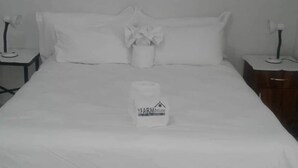 Une chambre d’hôtel avec un lit bien fait, une table de chevet avec une lampe et une petite table de nuit avec une lampe.