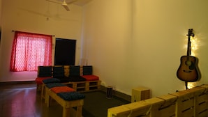 A room with a ceiling fan, a guitar, a red curtain, and a wooden bench. - Shepherd Stories - Hostel (Hyderabad)